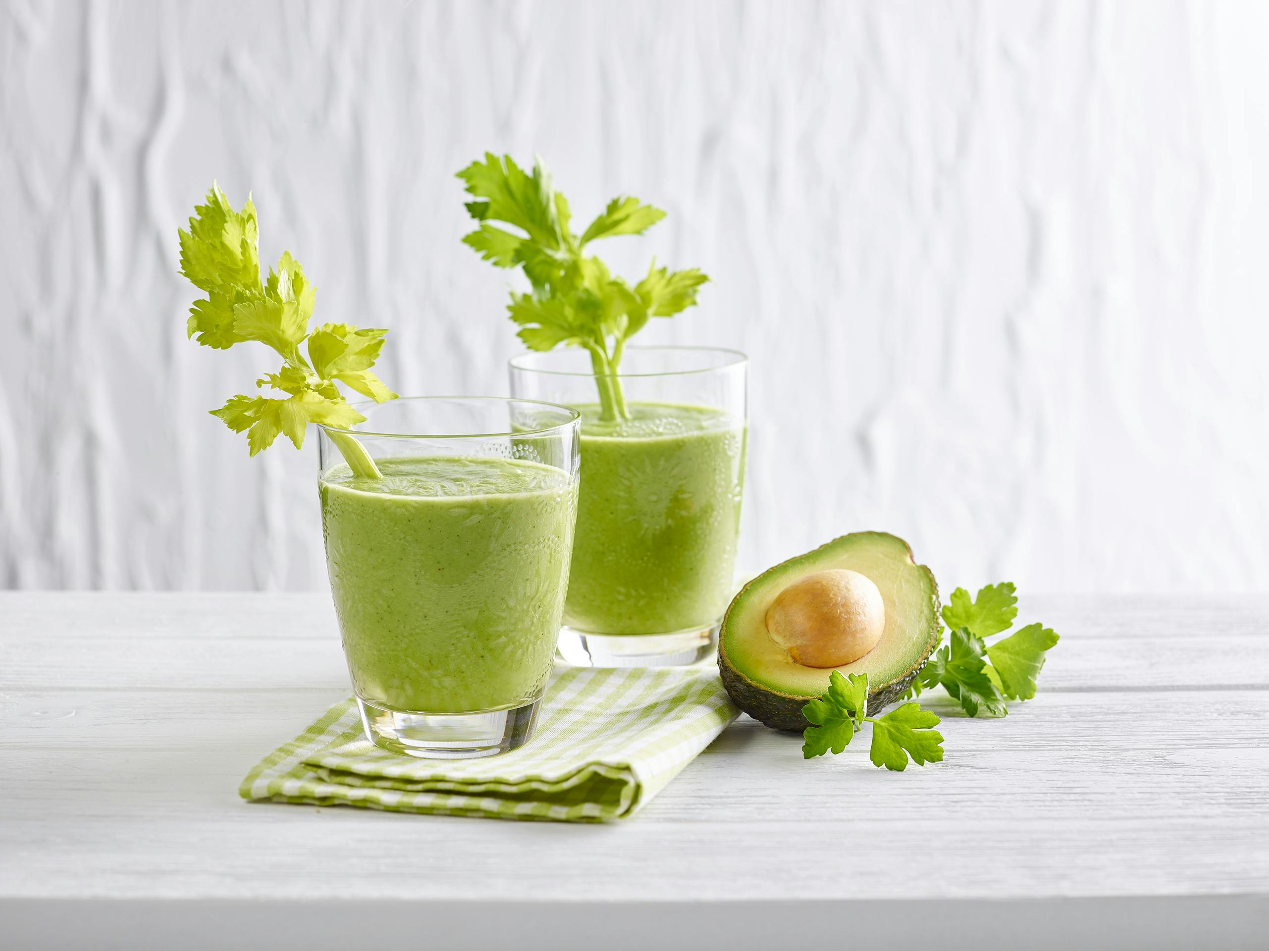 Green Smoothie mit Petersilie und Avocado in 2 Gläsern mit einer Selleriestange angerichtet