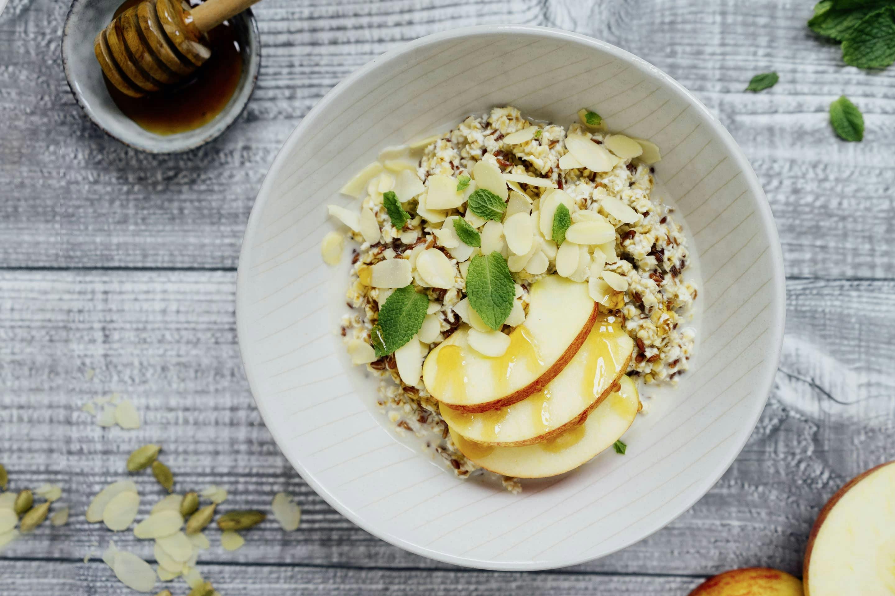 Overnightoats mit Cardamom und Apfelscheiben sowie Mandelblättchen mit Honig beträufelt in einer hellen Schüssel