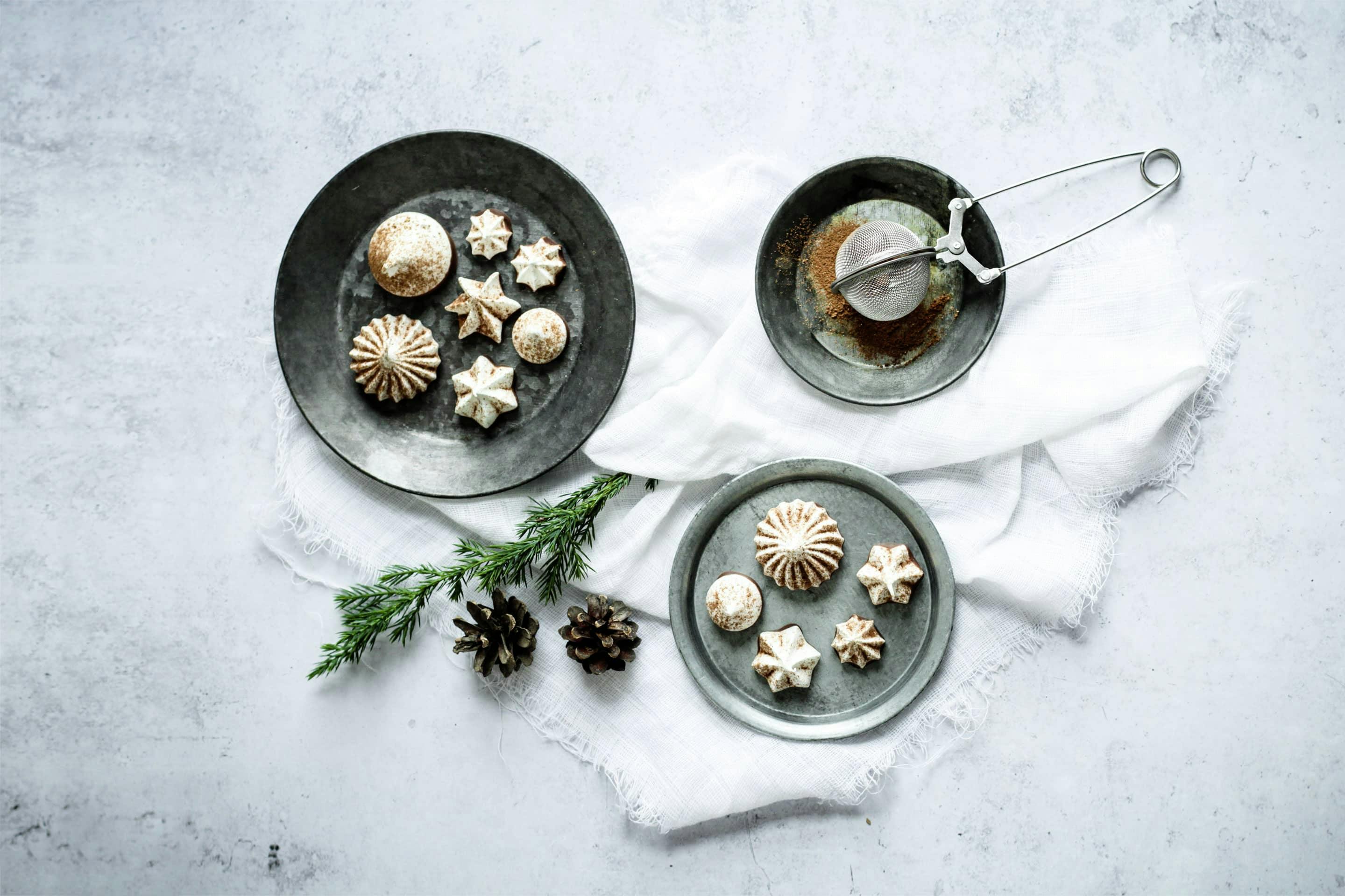 Chai-Baiserküsschen auf hellgrauen Tellern mit Weihnachtsdekoration