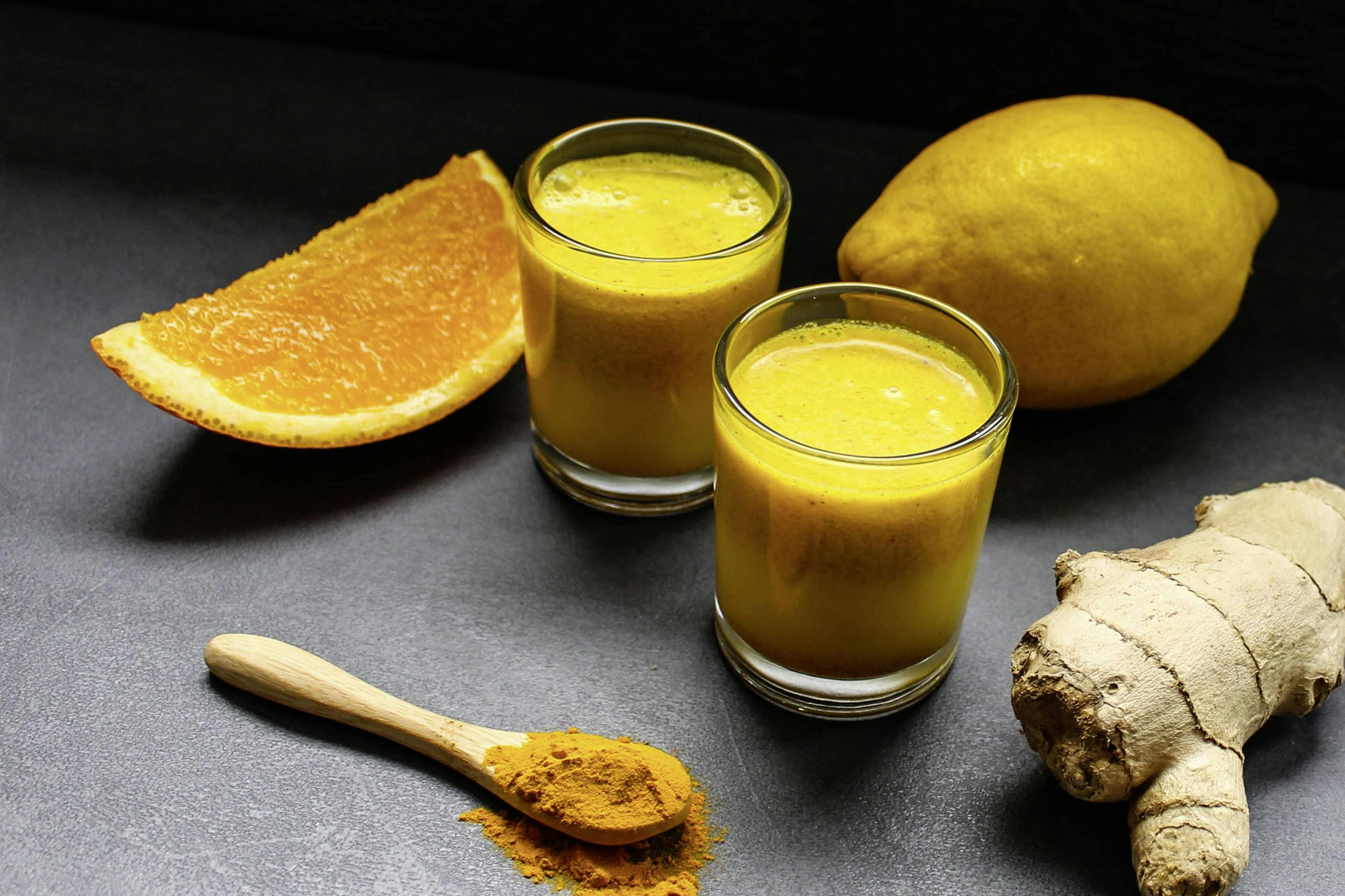 Ingwer-Curcuma Shot mit Zitrone und Orange in 2 Gläsern mit einem Löffel voll gemahlener Curcuma
