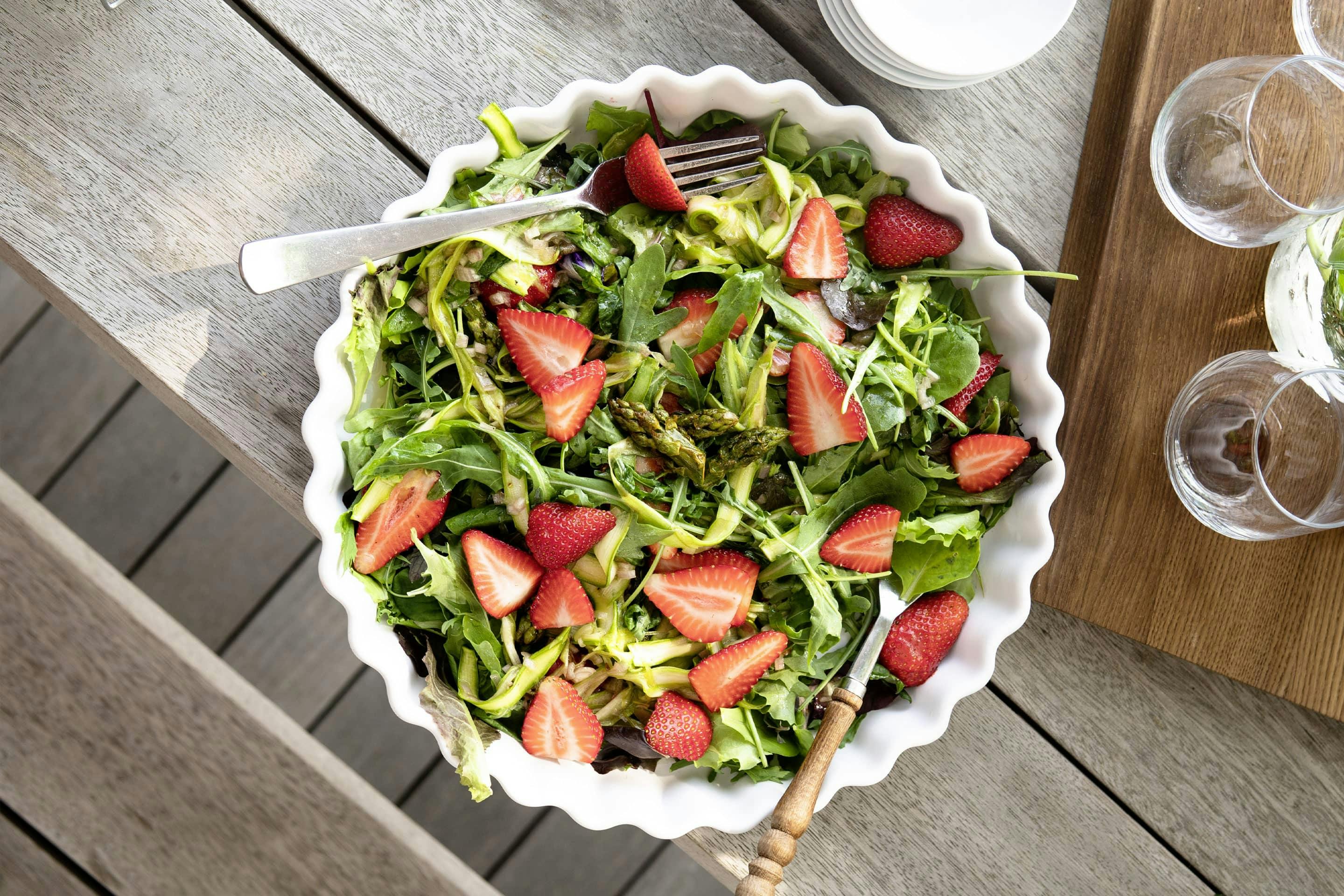 Erdbeer-Spargel-Salat mit Grillgewürzsalz in einer großen weißen Schüssel angerichtet und auf einem Holztische stehend.
