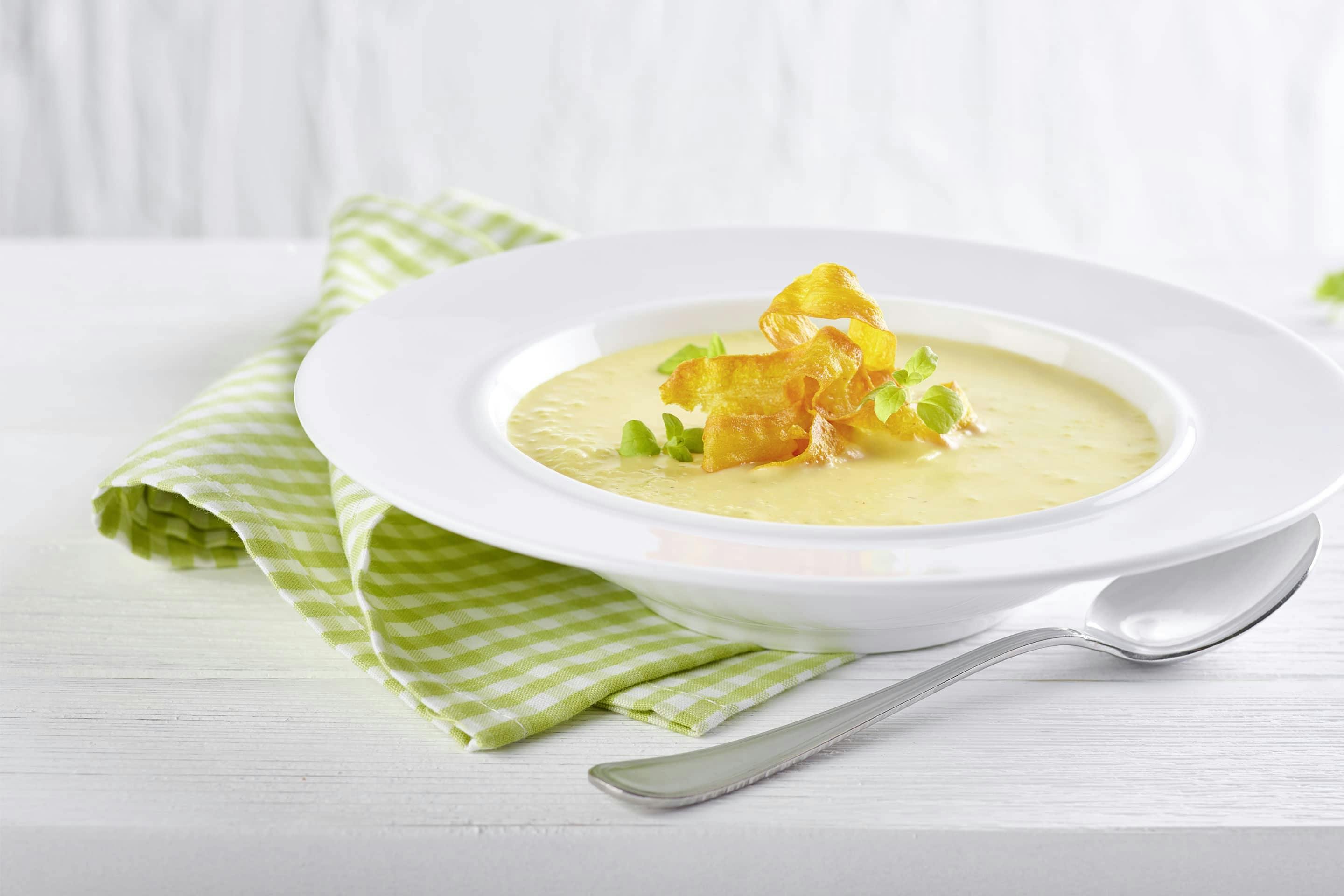 Karotten-Erdäpfels-Suppe mit Topping und frischen Kräutern in einem tiefen weißen Teller