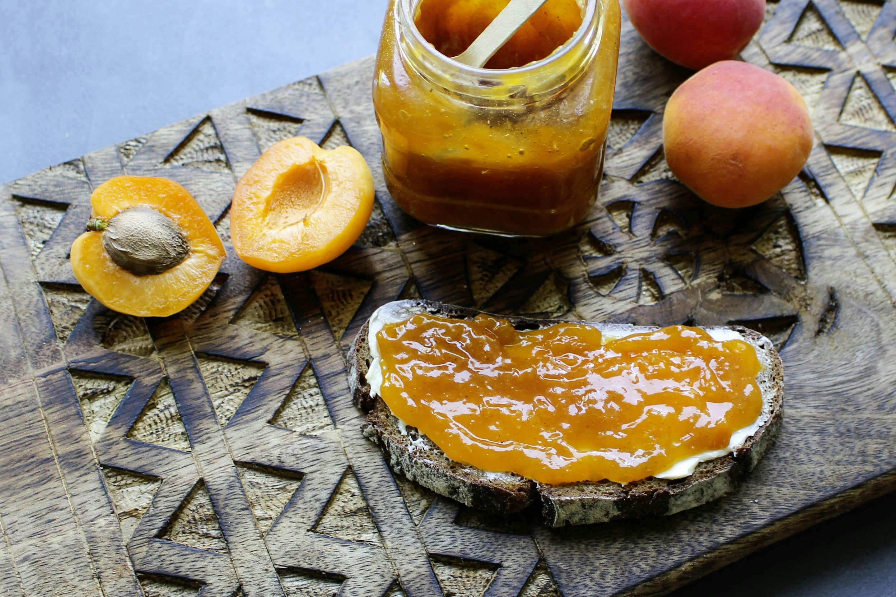 Marillenmarmelade mit Veggy Sweet in einem Marmeladenglas mit einem Brot und frischen Marillen auf einem Holzbrett