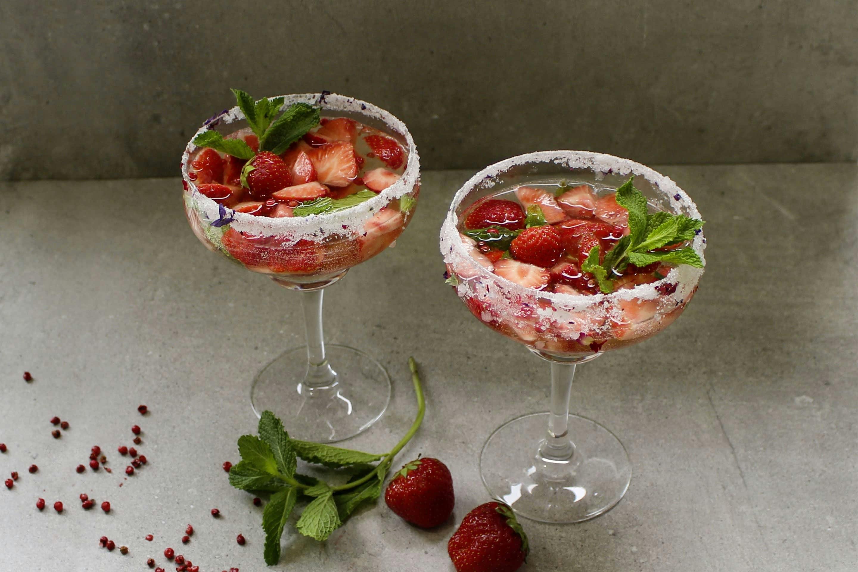 Sommer Bowle mit Rosa Beere und frischen Erdbeerstücken in gezuckerten Cocktailgläsern mit frischer Minze garniert