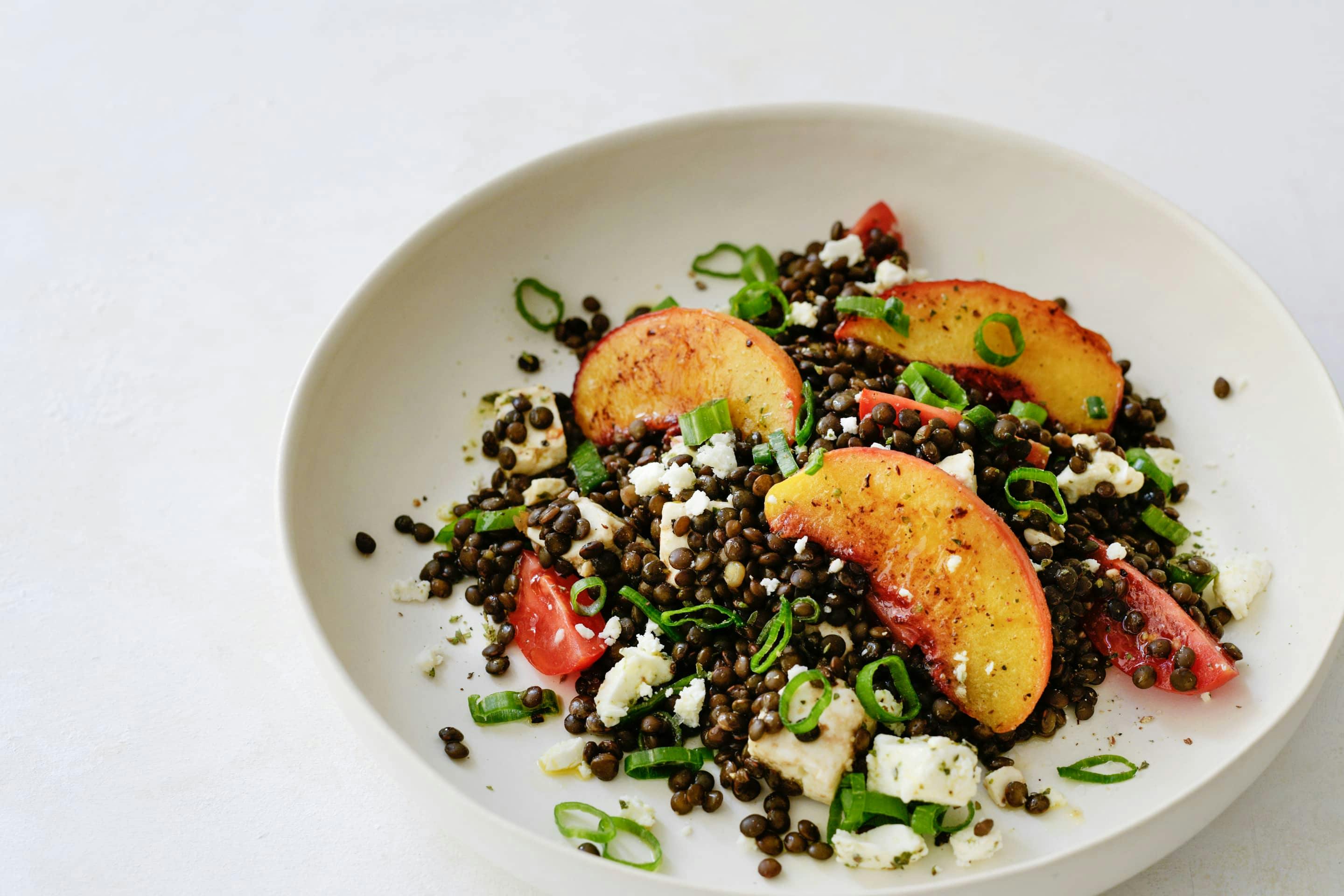 Belugalinsensalat mit Pfirsich und Feta und Bio-Majoran gewürzt in einem hellen tiefen Teller