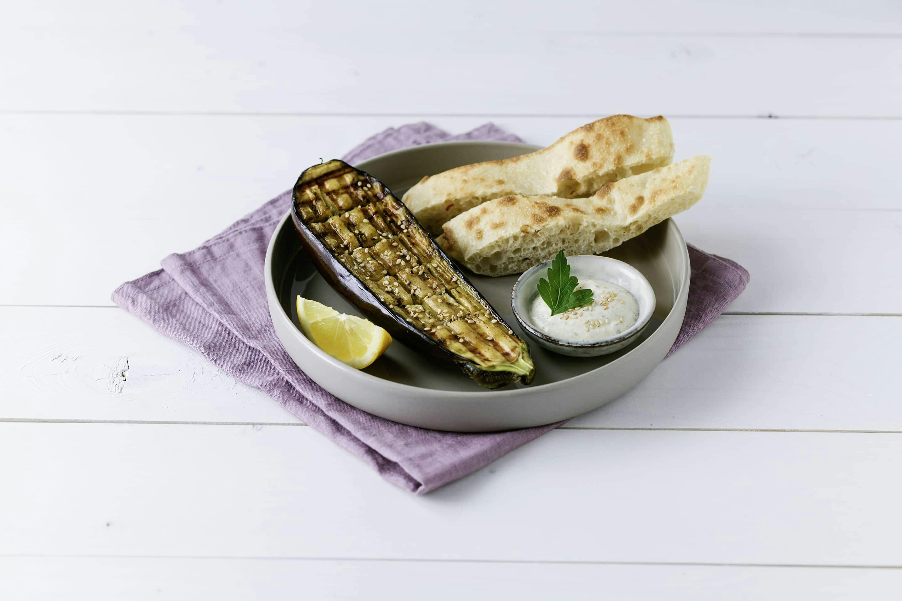 gegrillte Melanzani mit Pita und Sesam-Dip auf einem grauen Teller mit lilafarbener Serviette