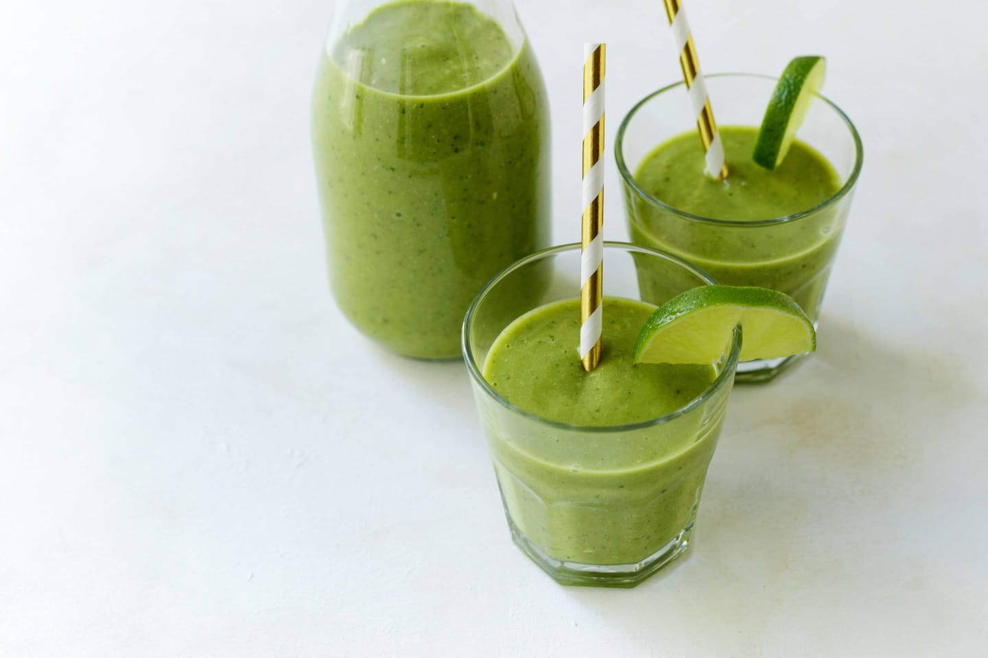 Grüner Smoothie mit Avocado, Ingwer und Curcuma in 2 Gläsern mit Stohhalm und einer Flasche