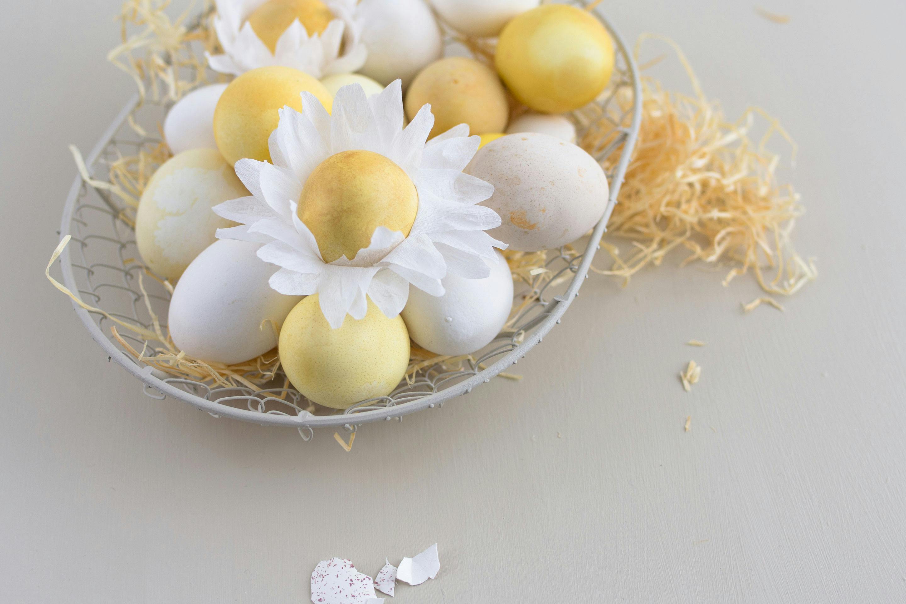 gefaerbte Eier in einem Körbchen, 2 mit selbstgebastelter Blüte aus Krepp-Papier