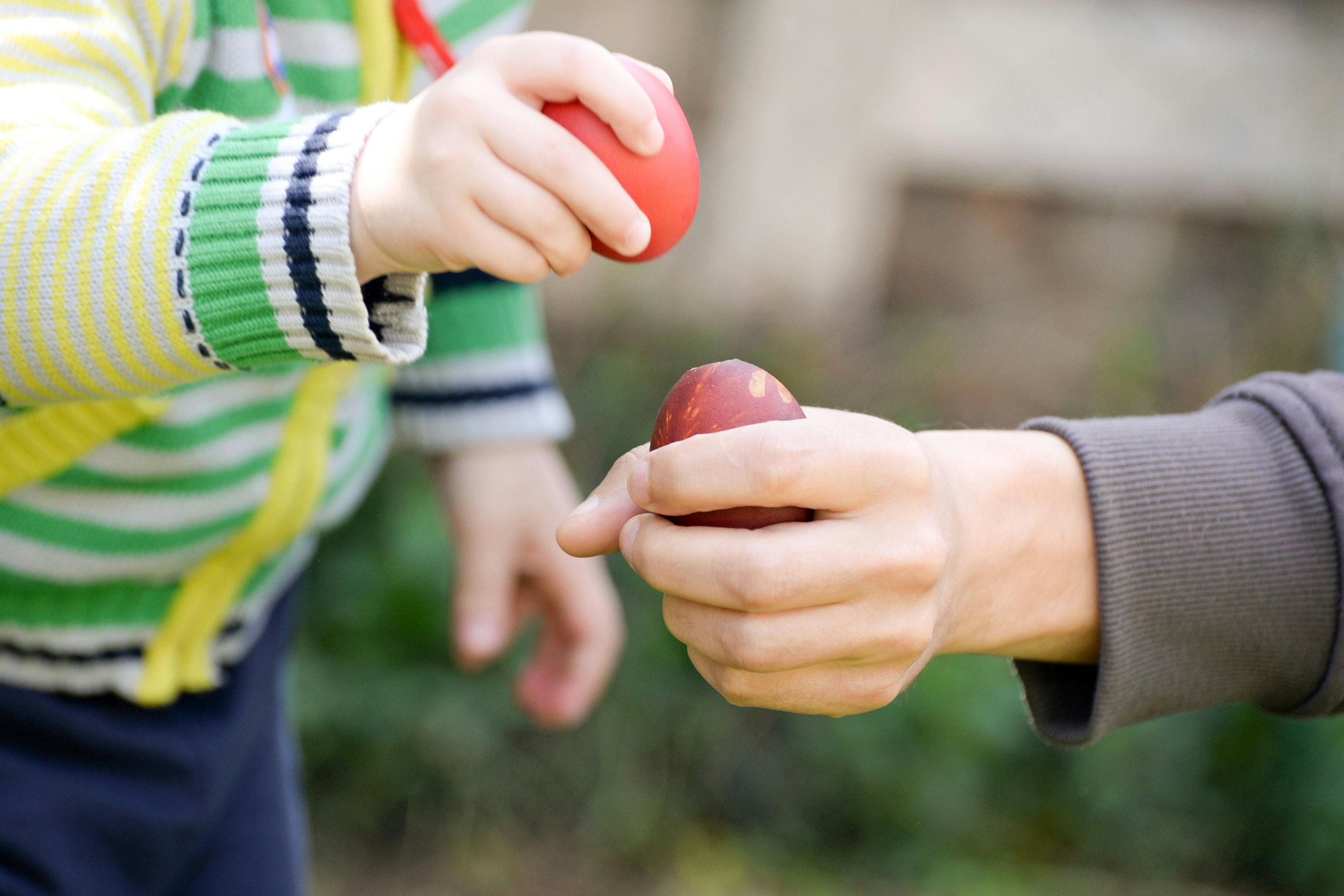 Kinder- und Erwachsenenhand haben ein Ei und klopfen es gegeneinander