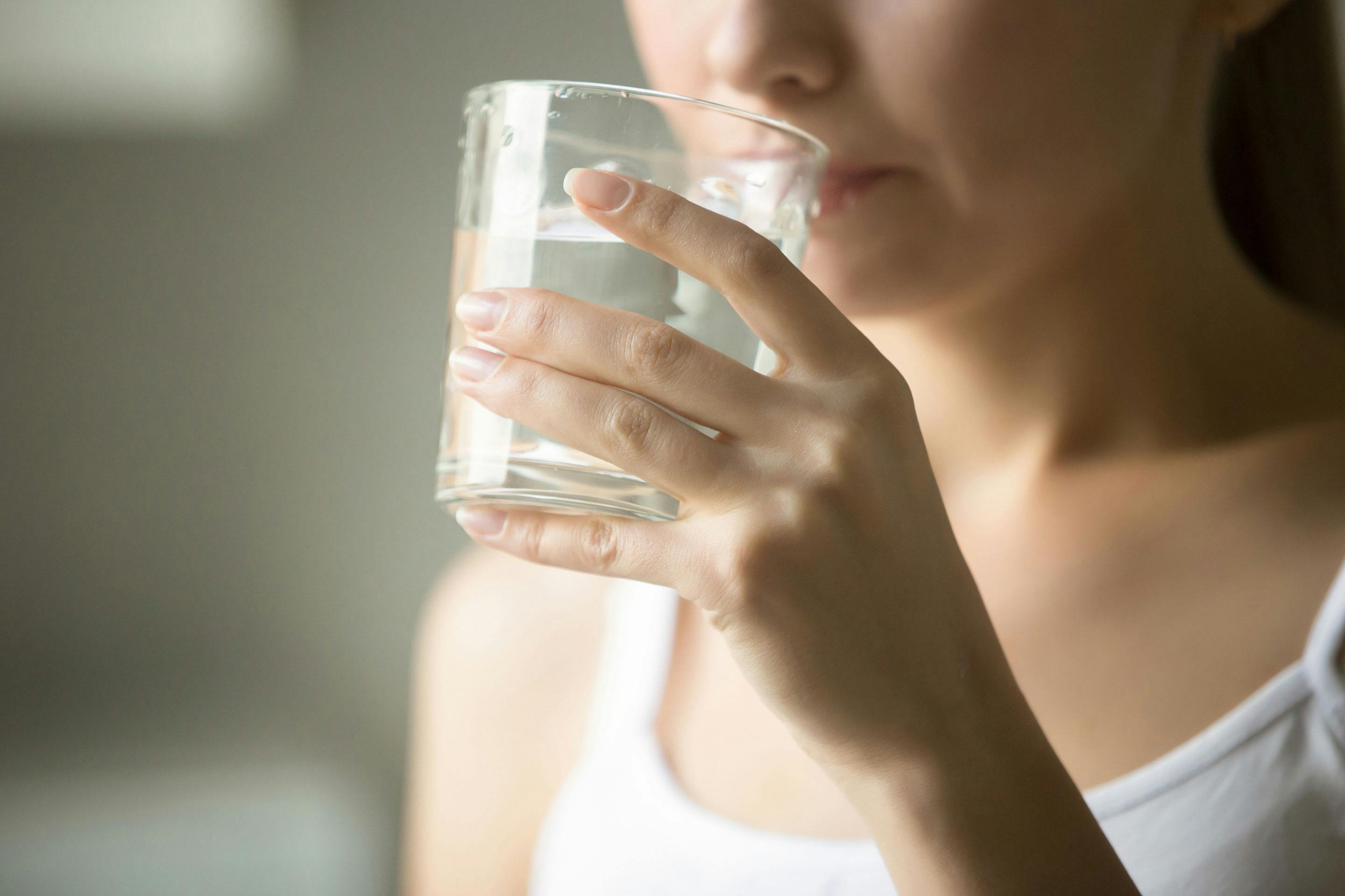 Frau in weißem Unterhemd trinkt Wasser aus einem Glas