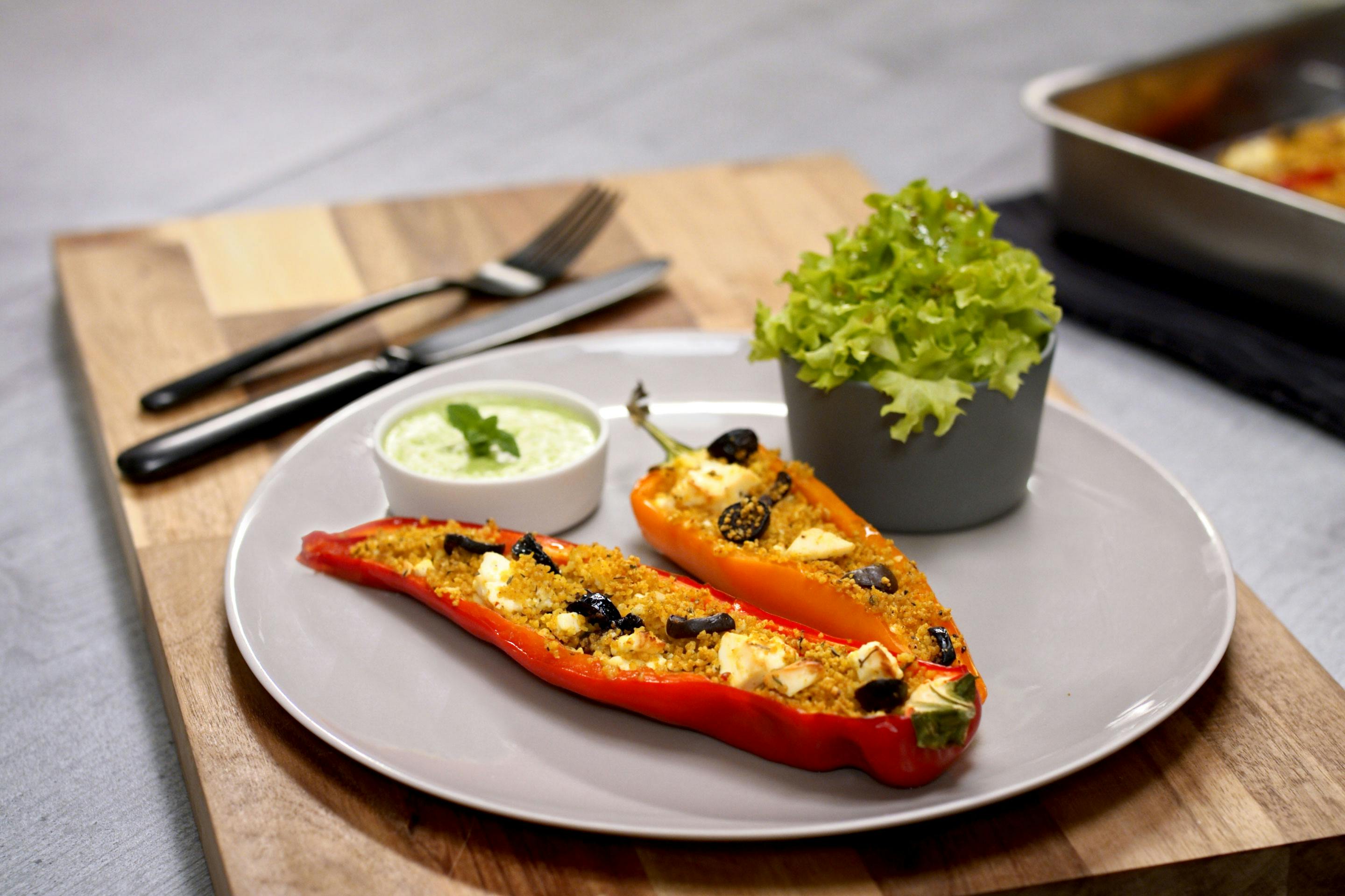 Gefuellte Paprika mit Couscous und Erbsendip, auf einem grauen Teller platziert; dazu gibt es grünen Salat in einem Schälchen