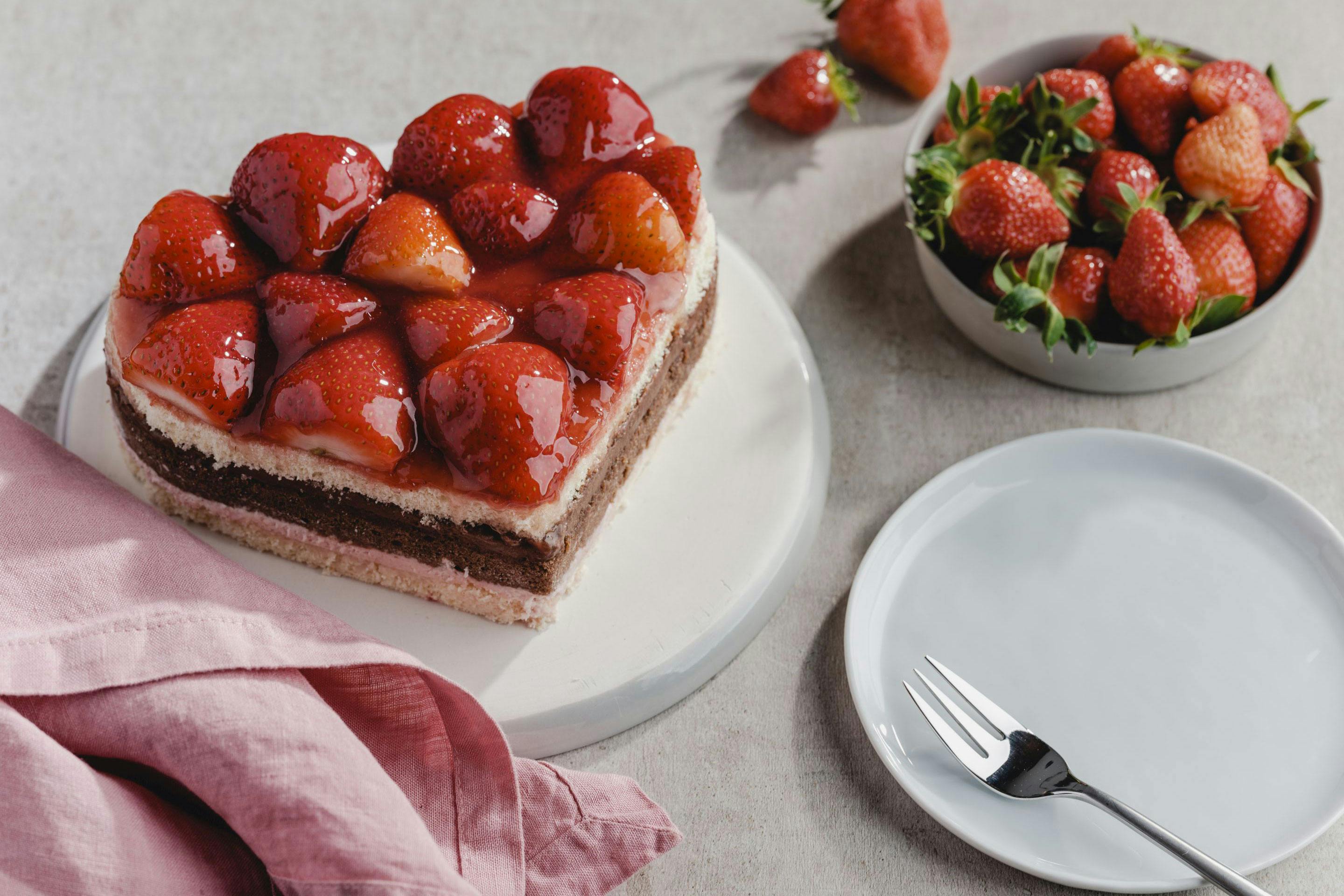 Erdbeer-Schokokuchen in Herzform und ein Schälchen mit Erdbeeren sowie Serviettte und Teller mit Kuchengabel