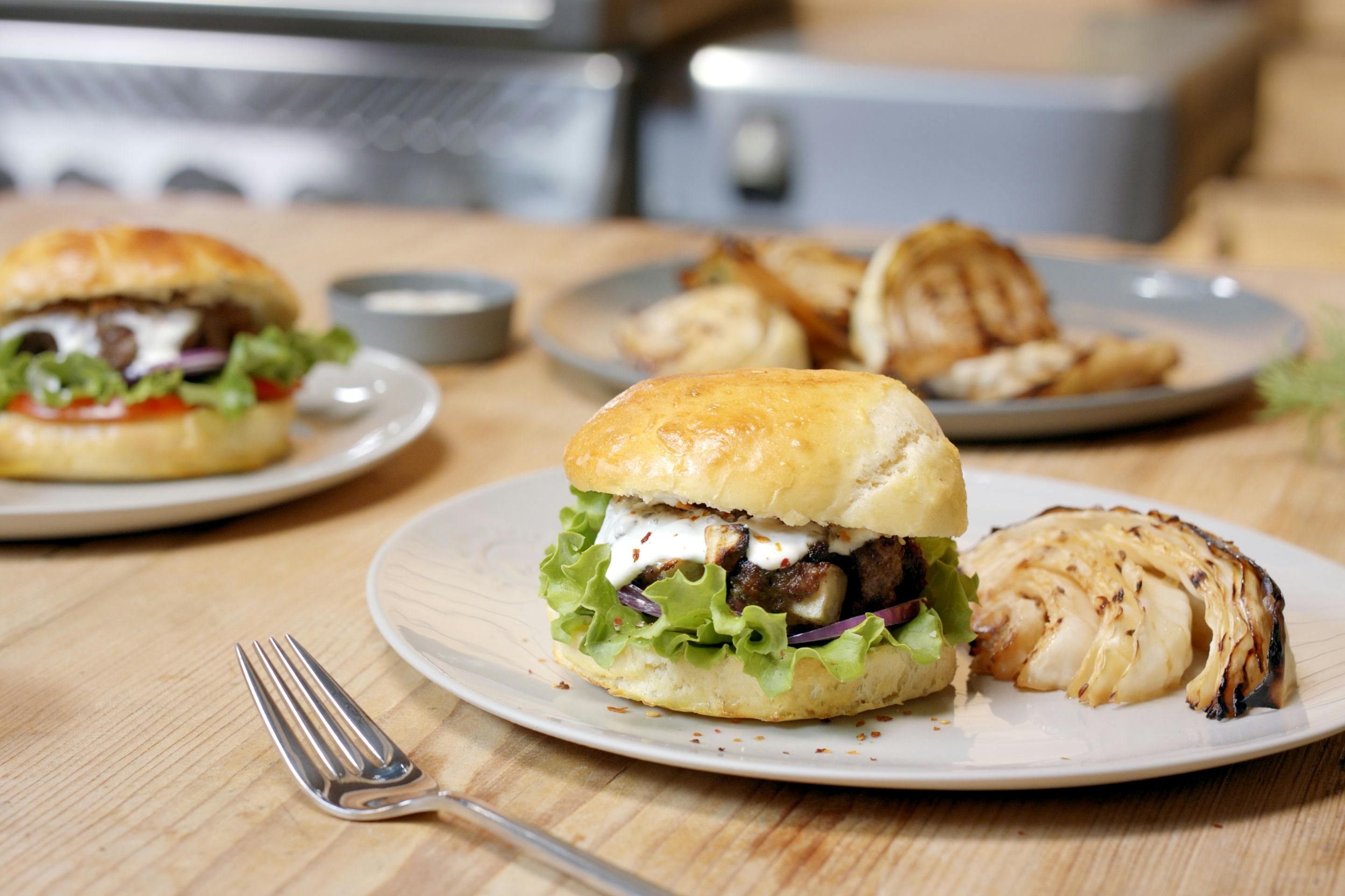 Burger mit Käse-Röstzwiebel-Patty und gegrilltem Krautkopf auf einem hellen Teller auf einem Holztisch