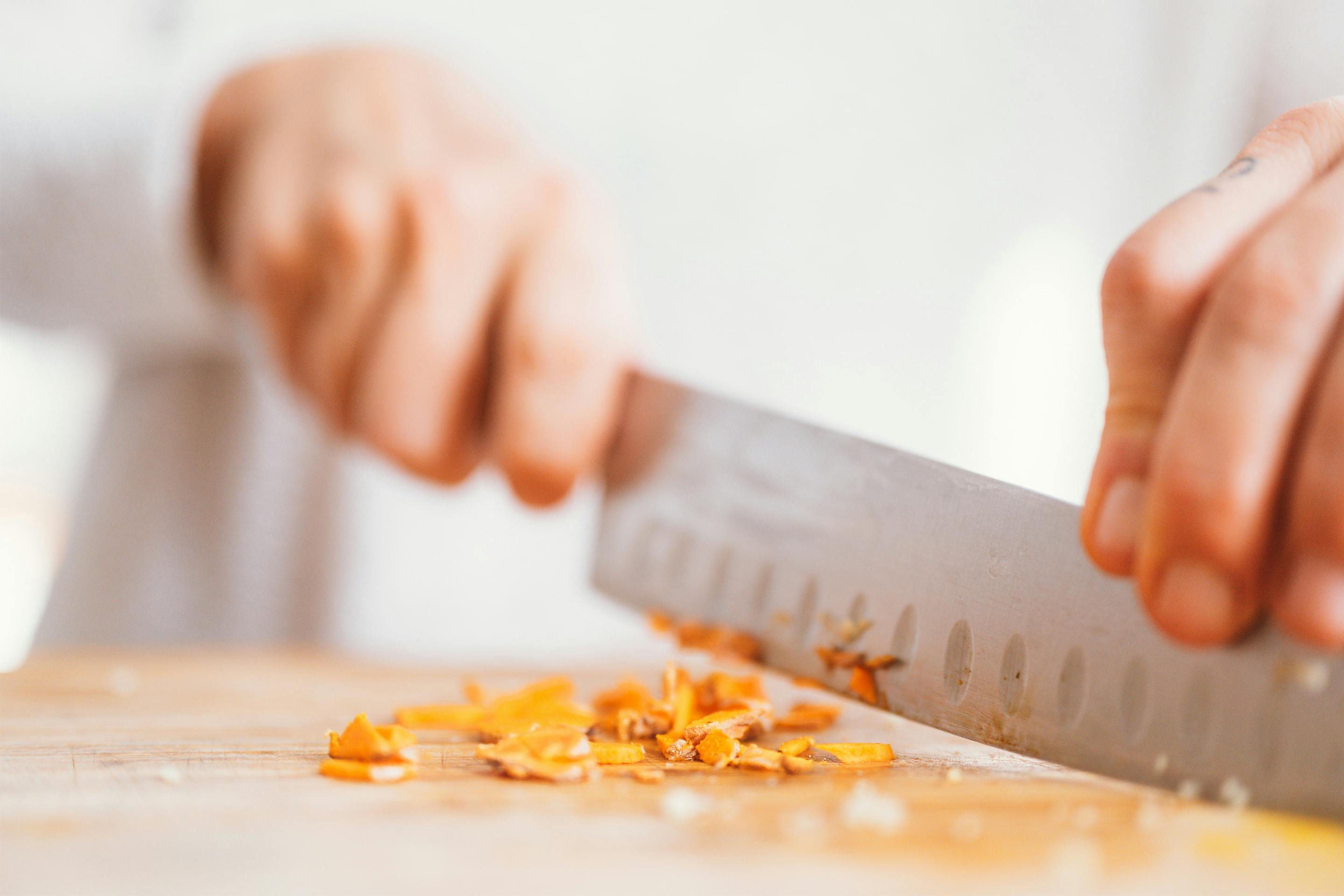 Frauenhand schneidet Curcumawurzel mit einem großen scharfen Messer