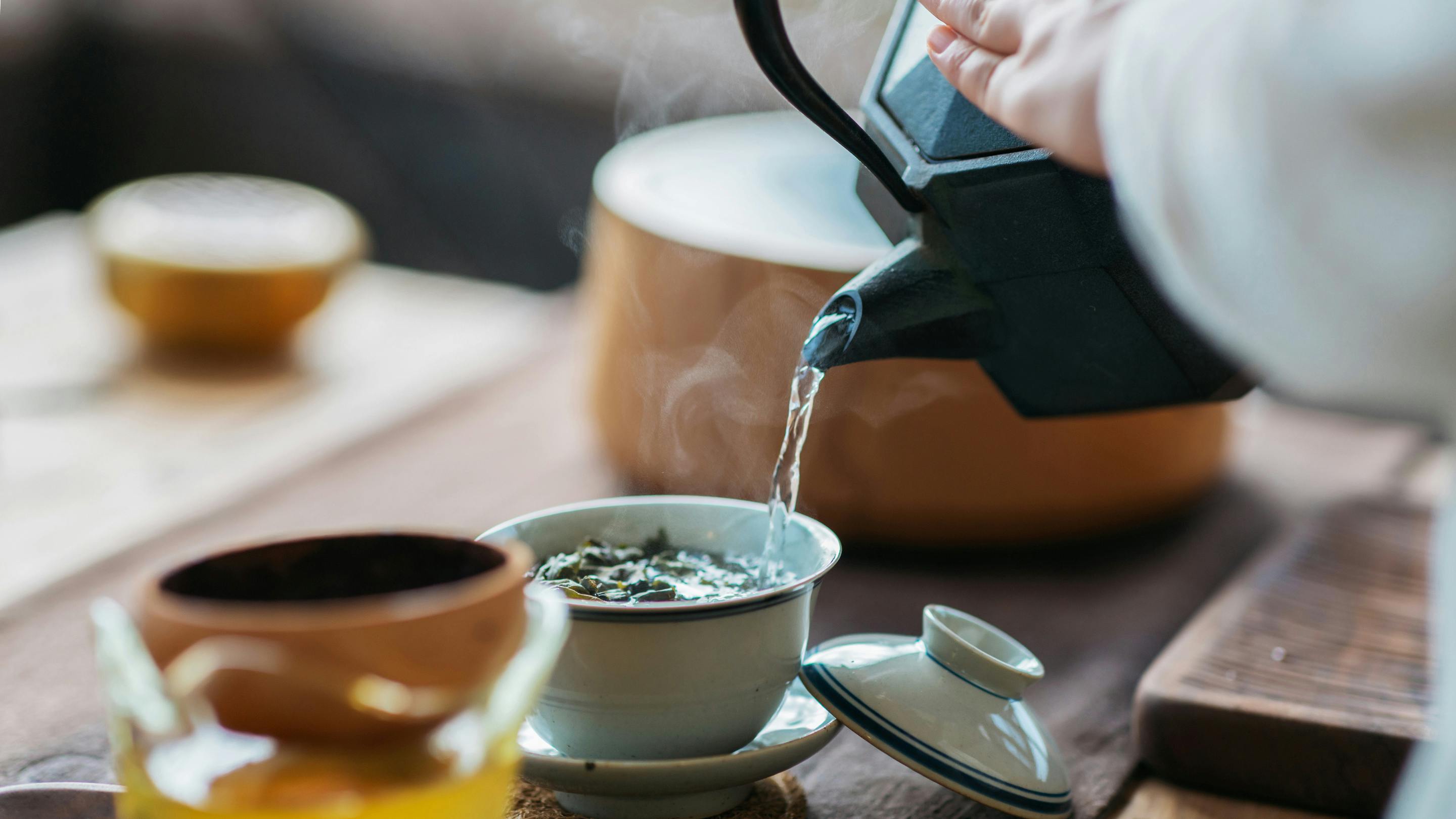 Frau gießt Tee aus einer schwarzen Kanne in eine helle Schale