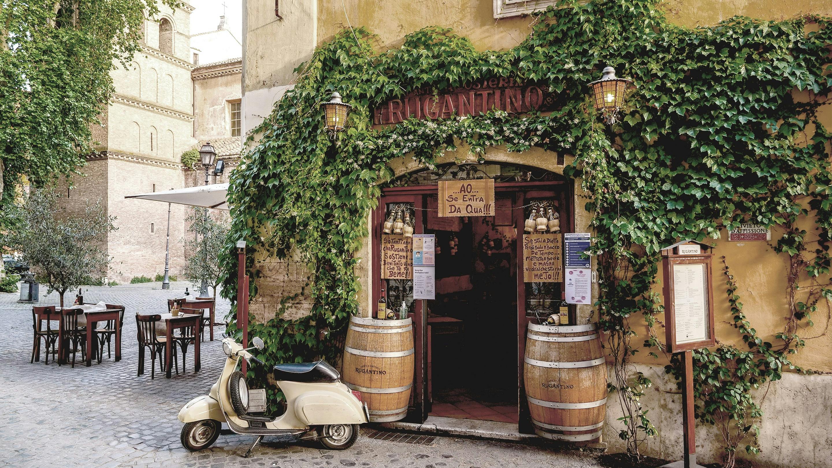 Eine Vespa steht vor einem kleinen italienischen Restaurant mit Gastgarten.