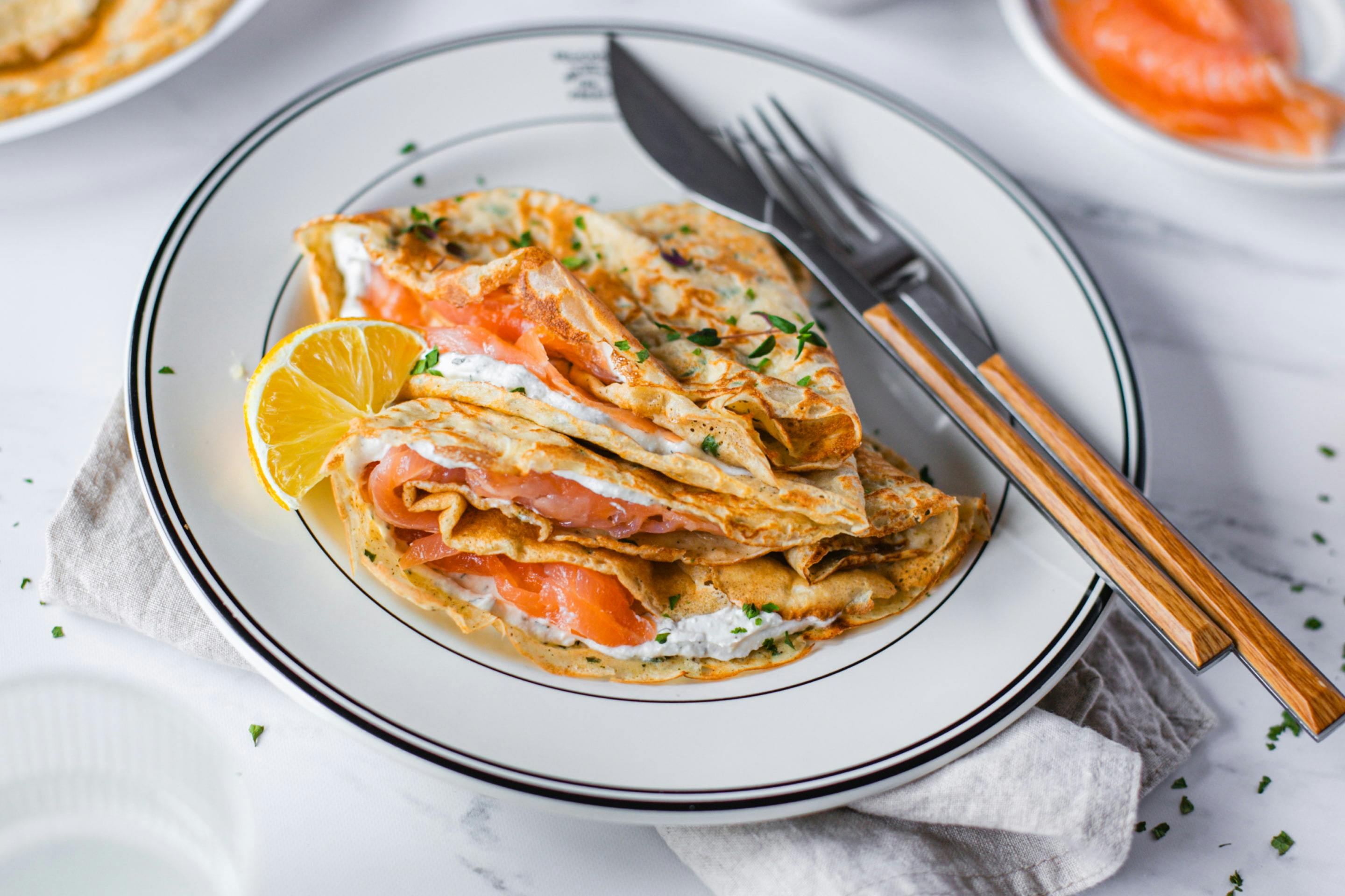 Kräutercrepes mit Räucherlachs, angerichtet mit Zitrone.